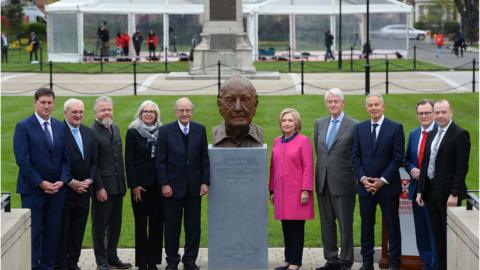 Attendees stand by the unveiled George Mitchell bust at Queen's University, Belfast.