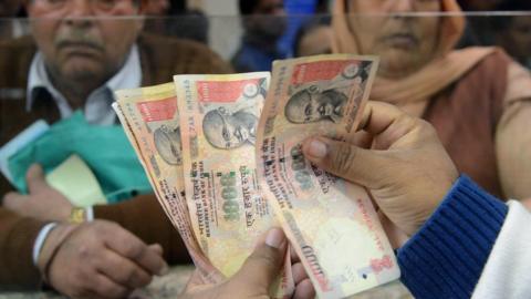 An Indian bank teller counts out notes as senior citizens gather inside a bank as they wait to deposit and exchange 500 and 1000 rupee notes in Amritsar on November 19, 2016.