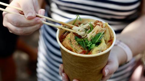 A woman holds a cup of laksa