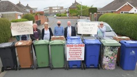 People lined up on a street with wheelie bins