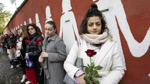 Students and university professors of the faculty of medicine and psychology observe 'a minute of noise' in memory of the victims of femicide, next to a mural depicting white silhouettes representing murdered women, in Rome, Italy, 05 December 2023.