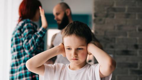 A boy covers his ears as parents argue