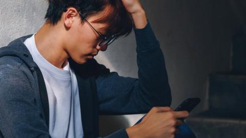 A stock photo of a young man looking at his phone upset