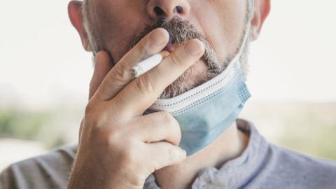 A man with a mask around his neck smoking