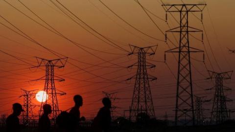 Locals walk past electricity pylons during frequent power outages from South African utility Eskom, caused by its aging coal-fired plants, in Orlando, Soweto, South Africa, September 28, 202