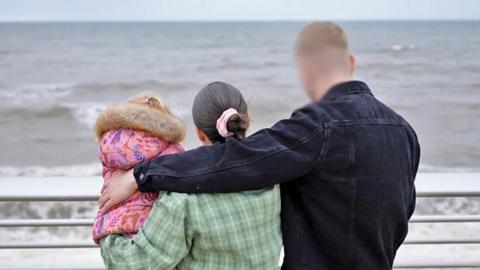 Amy and Peter with Rosie, in a photograph taken from behind, showing them looking out to sea