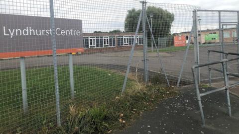 An exterior image of the Lyndhurst Centre in Swindon, through a chain fence