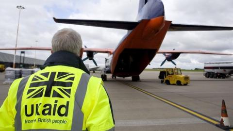 A Dfid employee wearing a UK aid hi-vis heads towards a plane