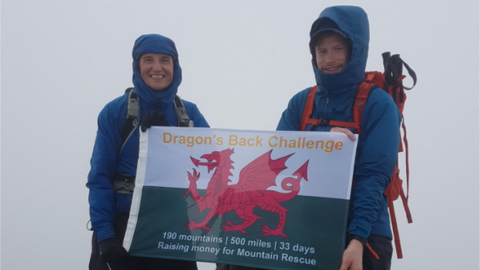 Mike and Matt standing with a flag at the top of Snowdon in the fog