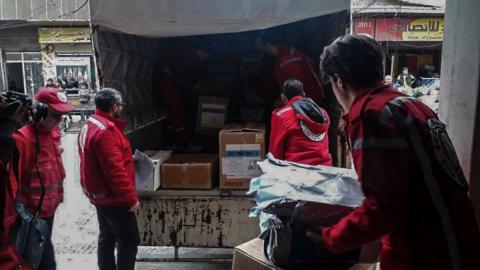 Six men working for the Syrian Arab Red Crescent unload boxes of supplies from the back of a truck