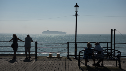 Couples on a pier overlooking the sea with a ship in the hazy distance