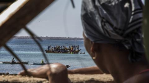 A woman watches as residents flee violence by boat