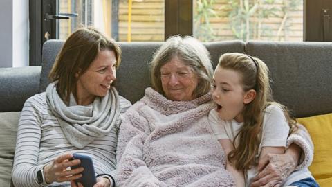 Mother, grandmother and daughter sitting on a sofa looking at a phone