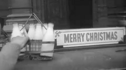 A milkman grabs bottles next to a Merry Christmas sign