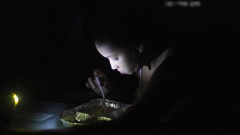 A woman eats under light from a torch