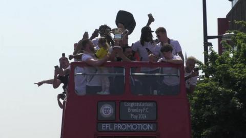 Bromley players raise a football cup as they travel through the town on a bus