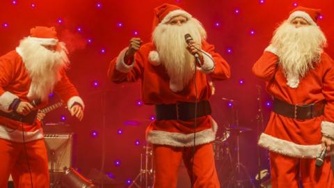 Three santas singing on stage