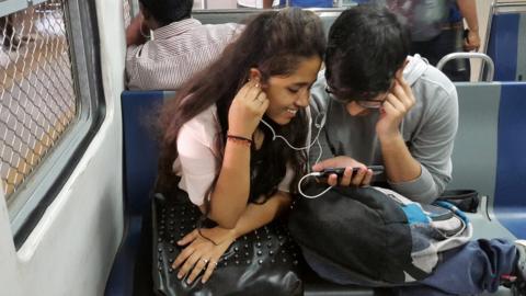 This photo taken on March 7, 2017 shows Indian students watching a movie on their smartphone while commuting on a suburban train in Mumbai. Buyouts, mergers and quick exits -- as India's richest man shakes up the country's ultra-competitive mobile market, telecommunications companies are scrambling to either consolidate or cut their losses and run.