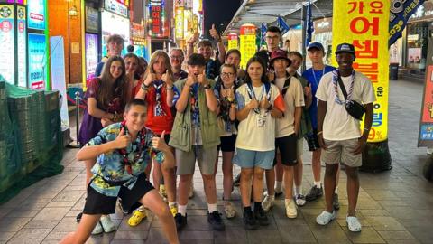 Henlow and Clifton Scout Group pose for the camera, thumbs aloft, in a Seoul street