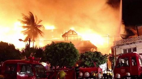 Hotel ablaze with firefighters in foreground