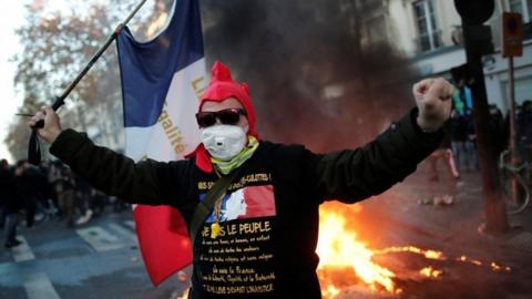A protester in Paris holds France's national flag in front of burning fire. Photo: 28 November 2020