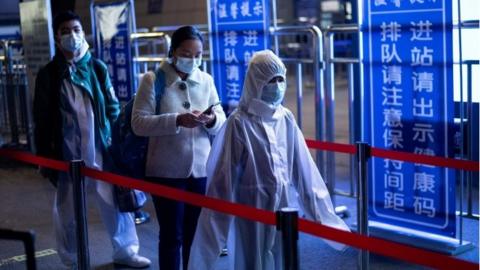 Passengers wear hazmat suits as they arrive at the Wuhan Wuchang Railway Station in Wuhan, to leave the city early on April 8, 2020.