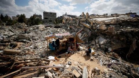 Palestinians sit in a makeshift tent amid the rubble of buildings destroyed in Israeli air strikes in Gaza (23 May 2021)