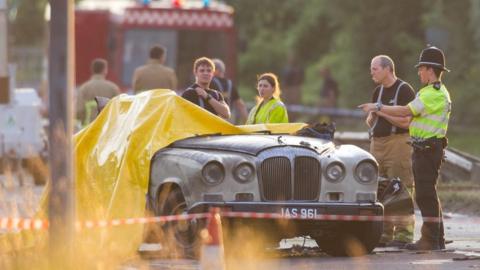 Police officers and Firefighters observe a Daimler wedding limo at the scene this morning as the sun comes up over the site. Hawker Hunter Plane Crashes During Display at Shoreham Airshow