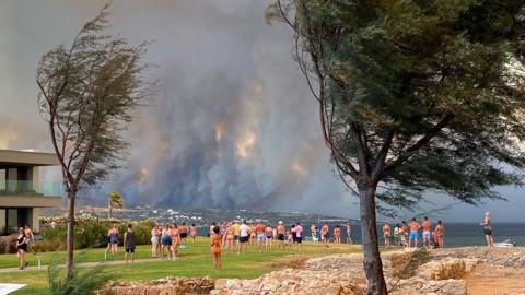 People looking at smoke billowing from a wildfire in Rhodes
