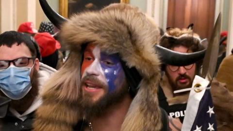 Jacob Anthony Chansley (C) is alleged to be the man seen wearing horns and a fur hat in photographs, including this from inside the Senate chamber