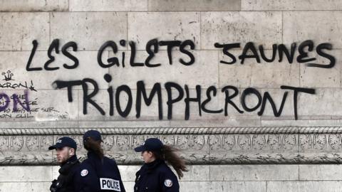 Police officers pass by a graffiti sprayed on the side of the Arc de Triomphe which reads "the yellow vests will triumph" as police and city employees assess the damages of the "Yellow Vests" protest a day earlier next to the Champs Elysee in Paris, France, 02 December 2018