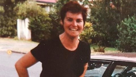 A young woman with short hair stands smiling outside an old car