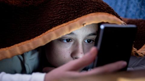 Teenage girl using her phone in bed