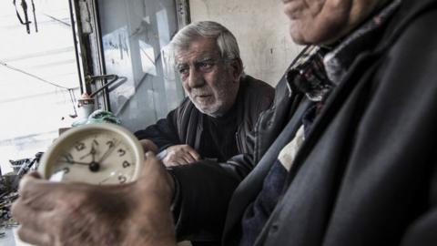A duo of clock and watch repairmen work in their small metal shop