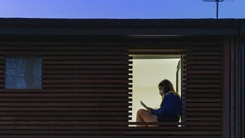 Girl wearing a face mask seen through a window - stock