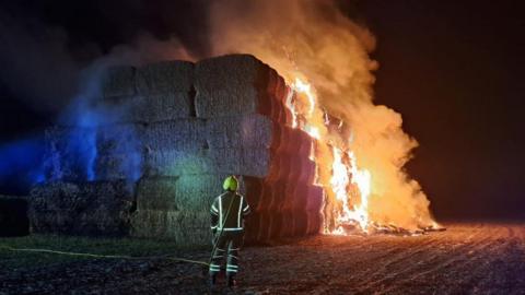 firefighter putting out fire on bales of hay