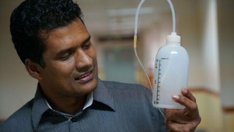 Dr Chisti holding a device made from plastic bottle and tubing