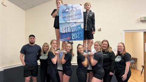 The cheerleaders pose to the camera with a big sign saying 'Winter weekender 1st place 2023'