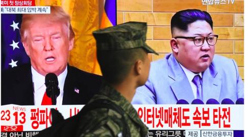 A South Korean soldier walks past a television screen showing pictures of US President Donald Trump and North Korean leader Kim Jong Un