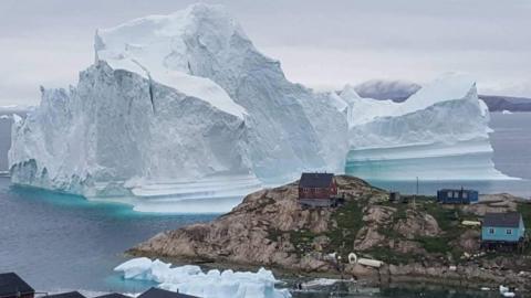 A giant iceberg is seen behind an Innaarsuit settlement, Greenland