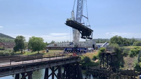 Crane lifts bridge section from its footings