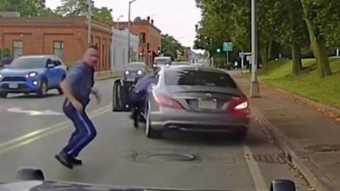 A Massachusetts state trooper clings on to car as it suddenly drives away