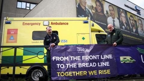 Ambulance staff hang up a union sign in front of an ambulance
