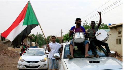Sudanese demonstraters wave their national flag as they celebrate in Khartoum early on August 3, 2019, after Sudan"s ruling generals and protest leaders reached a "full agreement" on the constitutional declaration.