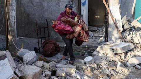 A man carries cushions through a building reduced to rubble.