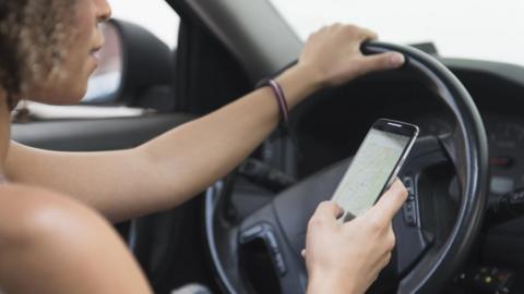 Woman looks at the phone she is holding while also driving