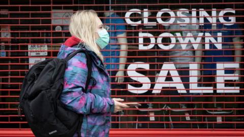 Woman with mask walks past closing store