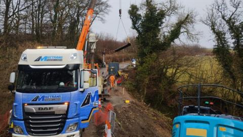 Contractors on site including a blue lorry and orange crane