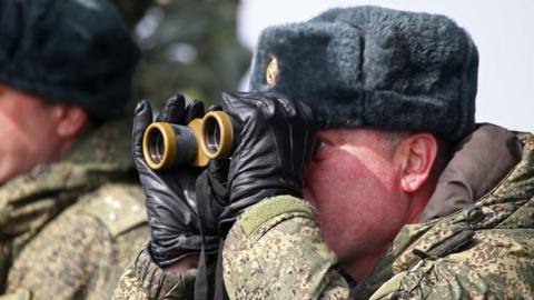 Russian solider looks through a pair of binoculars