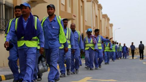 A line of men in high-vis vests walk at a football stadium construction site in Qatar